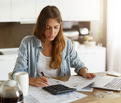 Une femme avec une chemise à carreaux qui fait ses factures avec une calculette